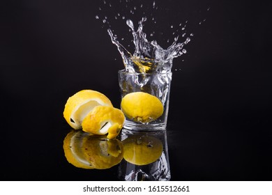 Slice Of Lemon Is Thrown Into A Glass. Peeled Piece Lies Nearby. Water Spray Everywhere.