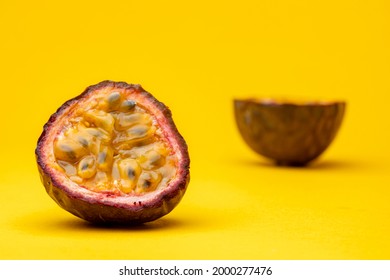 Slice of Maracuja or Brazilian tropical passion fruit showing the pulp flesh with out of focus the other half behind. Studio still life against a yellow background