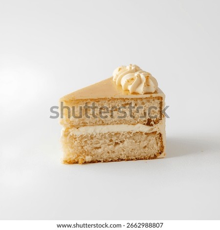A slice of moist vanilla sponge cake with creamy frosting, topped with delicate whipped cream rosettes. The golden glaze and soft texture highlight a minimalist