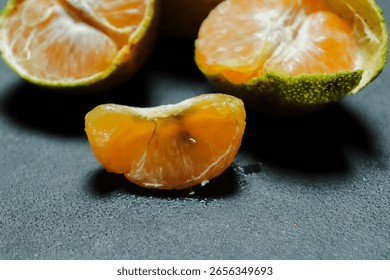 A slice of orange is on a table next to a whole orange. The slice is cut in half and has a green stem