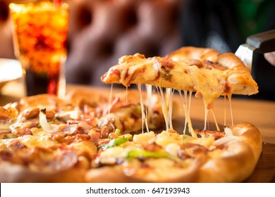 Slice Of Pizza Cheese Crust Seafood Topping. With Bell Pepper Vegetables Delicious Tasty Fast Food Italian Traditional And Soft Drink Carbonated With Men Sitting On Wooden Board Table Background Sofa.