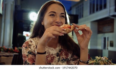 Slice Pizza In Hands Girl In Street Cafe At Night. Face Portrait Young Beautiful Woman With An Appetite Eating Slice Pizza With Salami And Tomatoes.