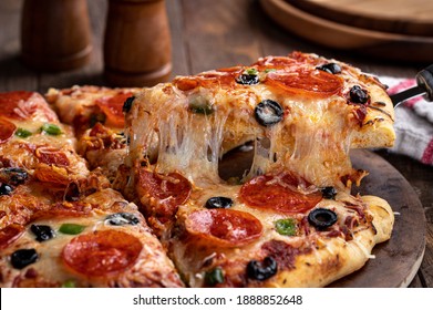 Slice Of Pizza With Pepperoni, Olives And Green Peppers On A Serving Utensil.  Closeup Of A Cheese Pull