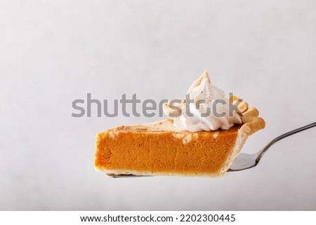 Slice of pumpkin cheesecake swirl pie topped with whipped cream being held on a spatula on light background