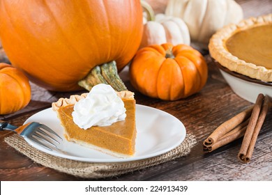 Slice Of A Pumpkin Pie And Pumpkins On Wooden Table