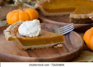 Slice Of Pumpkin Pie And Whipped Cream Topping With Pumpkin And Sliced Whole Pie In Background