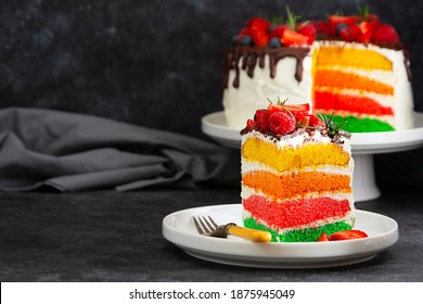 Slice of rainbow cake with fresh berries over dark background.