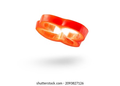 A slice of red paprika falls on a white backdrop. Red bell pepper flying in air on isolated white background