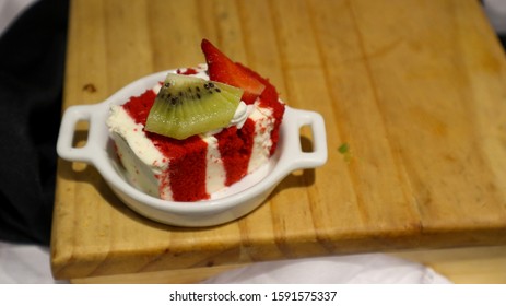 A Slice Of Red Velvet Cake Topped With Kiwi Pieces On Wooden Table, View From Above, Close-up