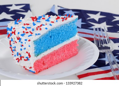 Slice Of Red, White And Blue Layer Cake On A Plate With American Flag Napkins