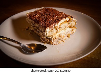 Slice Of Tiramisu Made Of Coffee, Chocolate, Mascarpone, Sponge Cake And Cream On A Plate With A Spoon