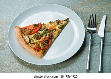 Slice Of Veggie Pizza On Gray Plate. Knife And Fork Near The Dish On Stone Anthracite Color Background. Piece Of Vegetable Pizza With Tomatoes, Champignon Mushrooms, Sliced Eggplant With Pesto Sauce