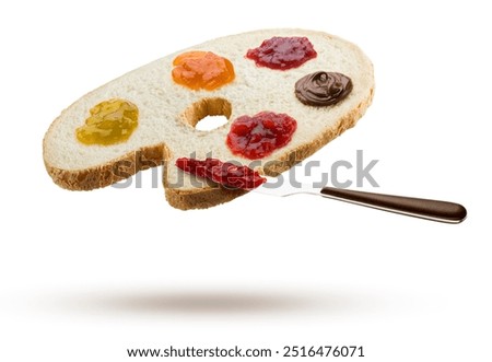Slice of white bread shaped like a painter's palette with variety of jam spread and knife flying on white background.
