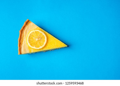 Slice Of Yellow Lemon Cake Decorated With A Slice Of Lemon, On A Blue Background. Directly Above View. Minimalist Style. Delicious Fruit Dessert.