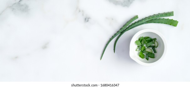 Sliced aloe vera leaves on marble background. Ingredients for natural organic cosmetic cream or lotion. Flat lay, top view. 