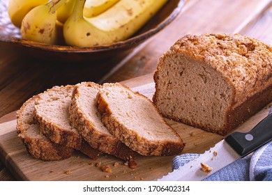 Sliced Banana Nut Loaf Cake On A Wooden Cutting Board With Bananas In Background