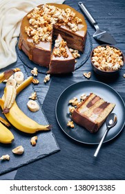 Sliced Banana Sponge Cake Layered With Peanut Butter Mousse And Topped With Chocolate Ganache, Melted Caramel And Sweet Popcorn, Vertical View From Above