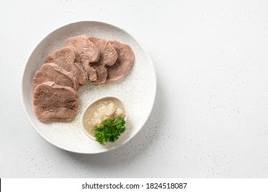 Sliced beef tongue delicacy with natural horseradish sauce isolated on a white table. View from above. Space for text.
