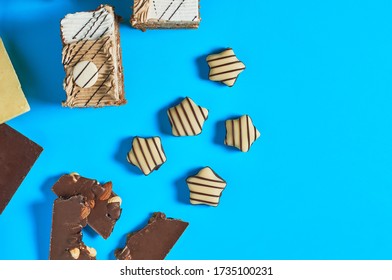 Sliced checkered rectangular cake near chocolate bar and candies lies on blue table on party. Celebration concept. Space for text. Top view - Shutterstock ID 1735100231