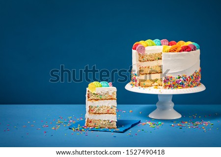 Sliced confetti Birthday cake  with rainbow colored icing and Sprinkles over a blue background.