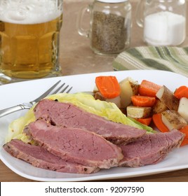 Sliced Corned Beef And Cabbage With Vegetables On A Plate And A Glass Of Beer In Background