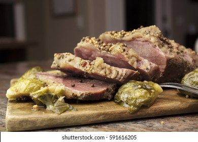 Sliced Corned Beef On A Wooden Cutting Board, Garnished With Pepper Corns And Brussel Sprouts Ready To Serve As A Party Platter