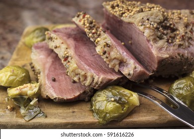 Sliced Corned Beef On A Wooden Cutting Board, Garnished With Pepper Corns And Brussel Sprouts Ready To Serve As A Party Platter