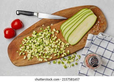 Sliced courgette zucchini vegetables on a wooden cutting board, knife, tomatoes, pink salt and napkin on a concrete light table. Top view Flat lat