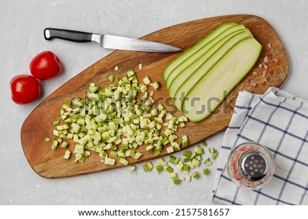 Sliced courgette zucchini vegetables on a wooden cutting board, knife, tomatoes, pink salt and napkin on a concrete light table. Top view Flat lat