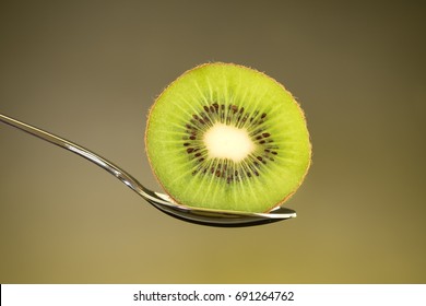Sliced Fresh And Juicy Green Kiwi Fruit On Spoon With Yellow Light Background, For Healthy Food And Fruit Salad Concept