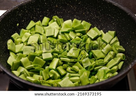 Sliced green asparagus beans lie on a black frying pan. Cooking. Background.