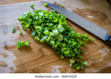 Sliced green onion stems on wooden cutting board, selective focus.