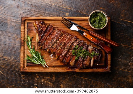 Sliced grilled beef barbecue Striploin steak with chimichurri sauce on cutting board on dark wooden background