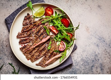 Sliced Grilled Beef Steak With Arugula And Tomato Salad In A White Plate, Dark Background.