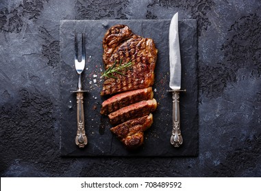 Sliced Grilled Meat Barbecue Steak Striploin With Knife And Fork Carving Set On Black Stone Slate