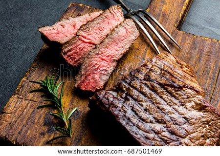 Sliced grilled medium rare beef steak served on wooden board Barbecue, bbq meat beef tenderloin. Top view, slate background.