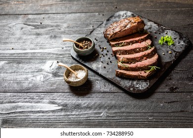 Sliced Grilled Roast Beef With Salt And Pepper On Marble Plate On Wooden Old Rustic Table Black Background. 