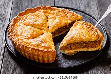 sliced Ground Beef Meat Pie with a flaky puff pastry double crust with hearty minced beef cooked with vegetables and seasoning on black plate on wood table, close-up