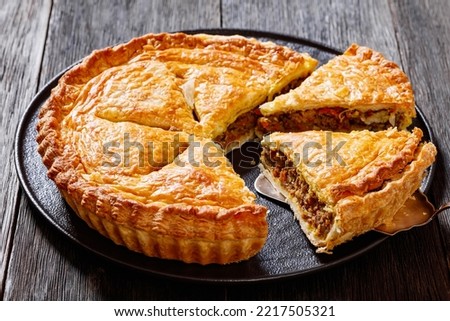 sliced Ground Beef Meat Pie with a flaky puff pastry double crust with hearty minced beef cooked with vegetables and seasoning on black plate on wood table