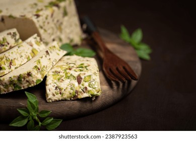 Sliced ​​turkish halva with pistachio on a wooden plate and rustic background. Traditional oriental dessert
