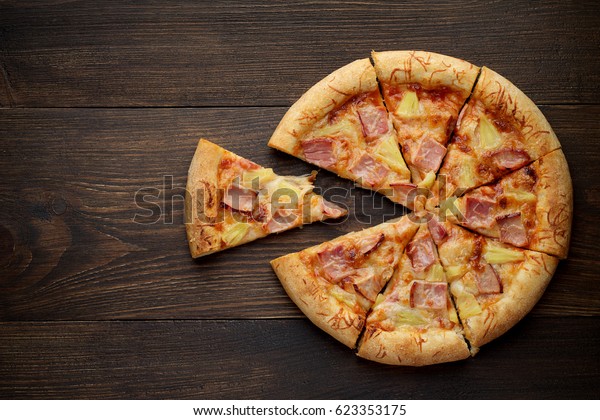 Sliced hawaiian pizza\
with pineapple and ham on dark rustic wooden background. Top view,\
copy space.