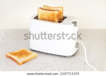 Sliced hot toasted bread for breakfast in modern white toaster on home kitchen table