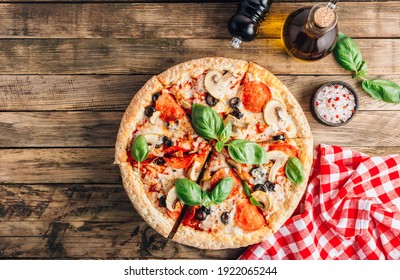 Sliced italian pizza with salami, mozzarella, mushroom, tomatoes, black olives and basil leaves on rustic wooden background. Italian traditional food. Popular street food concept. Top view - Powered by Shutterstock