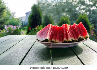 Sliced juicy red watermelon on a platter on a garden table against the backdrop of a garden on a bright sunny day. - Shutterstock ID 1808242360