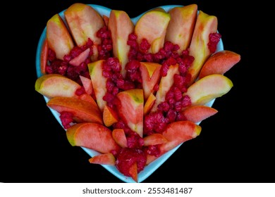 Sliced kissabel apple sprinkled with frozen raspberries served in heart shaped ceramic bowl against black background. Hidden rose apples, pink inside apple  - Powered by Shutterstock