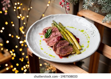 Sliced Kobe Rare Steak With Blood Garnished With Roasted Asparagus Top View In Winter Restaurant