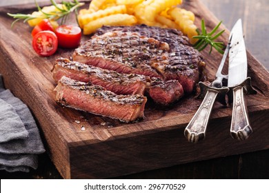 Sliced medium rare grilled Steak Ribeye with french fries on serving board block on wooden background - Shutterstock ID 296770529