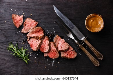 Sliced medium rare Roast beef with table knife and fork for meat on dark background