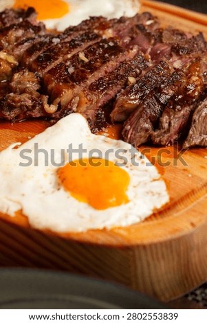 Sliced medium-rare beef steak with two fried eggs served on a wooden board.