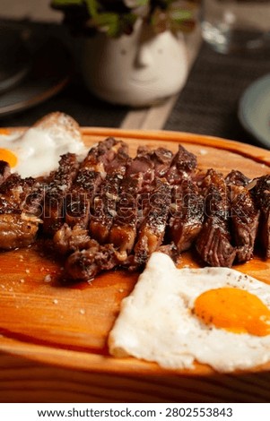 Sliced medium-rare beef steak with two fried eggs served on a wooden board.